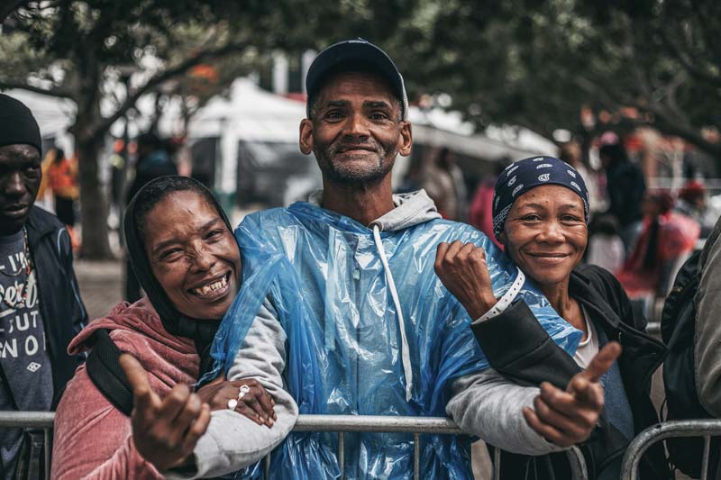 Three soup kitchen guests smiling whilst queueing for soup at a charity in Cape Town