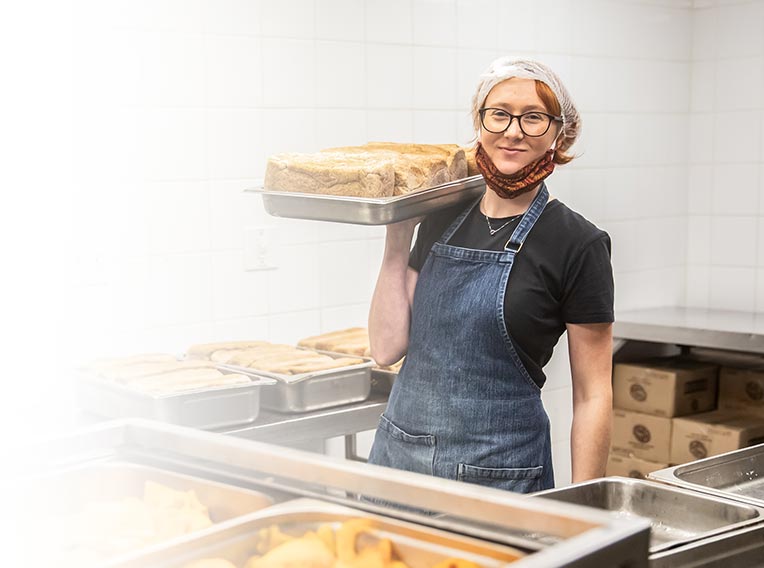 Volunteer in the charity kitchen holding a tray of freshly baked bread