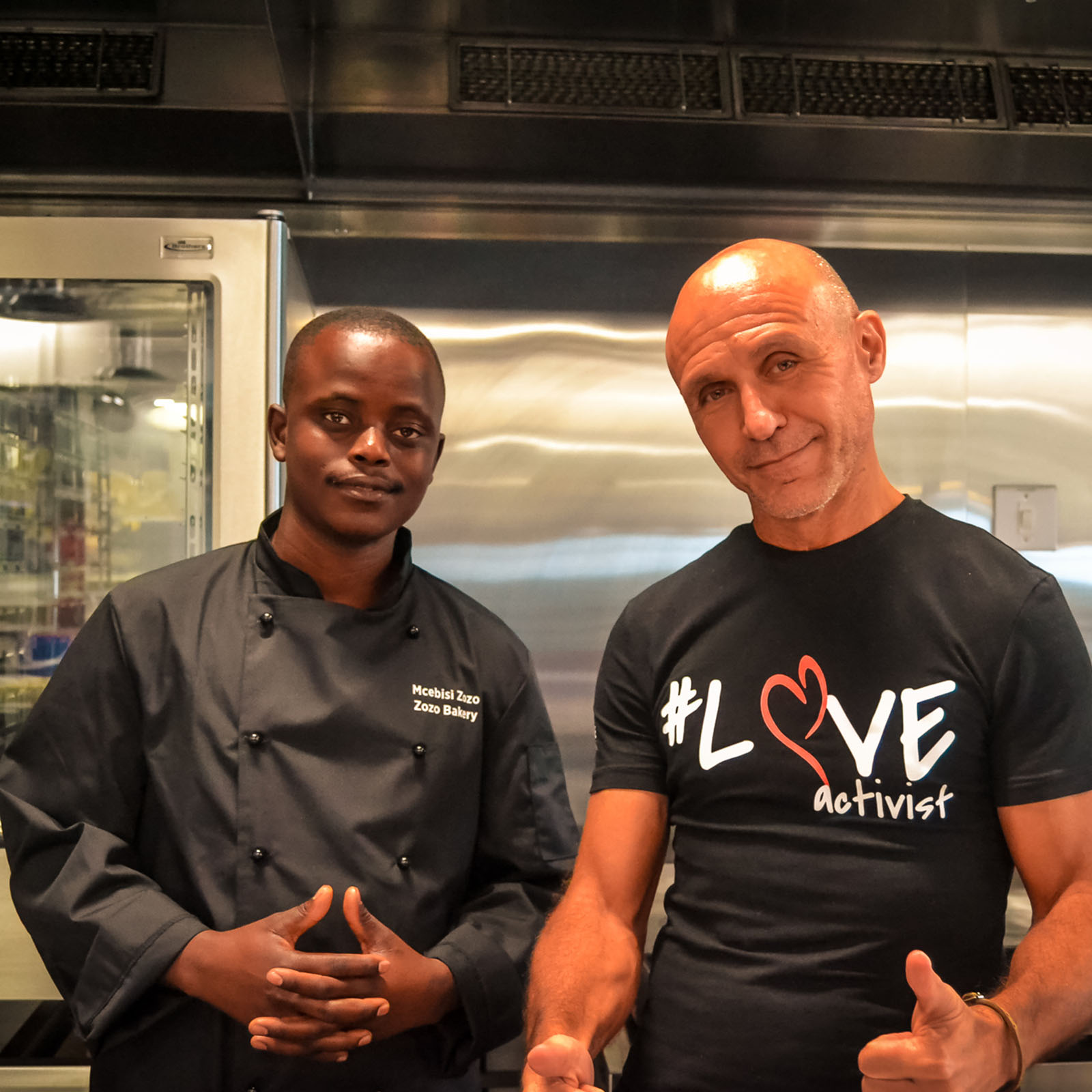Danny, Ladles of Love founder, standing with young food entrepreneur and baker, Mcebisi in a kitchen.