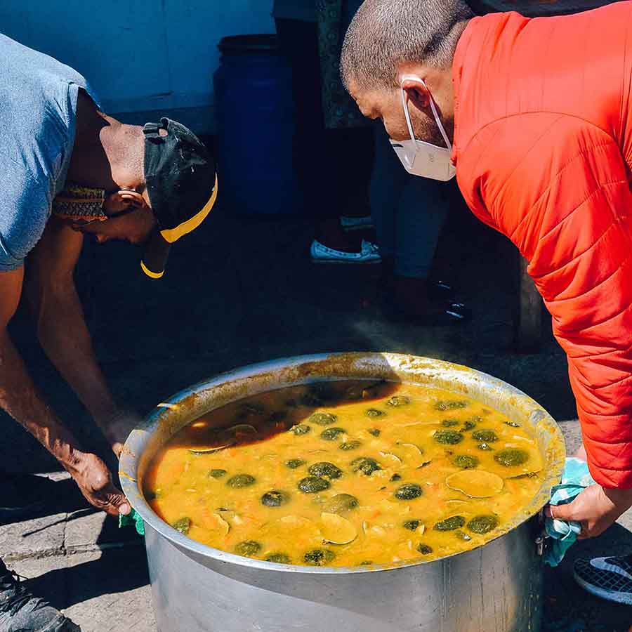 men holding a big pot of vegetable stew at a soup kitchen in cape town who rely on sustainable living charities to help grow more food