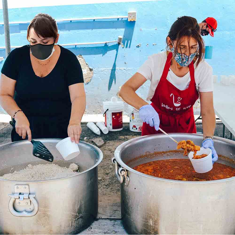 two women volunteering at a soup kitchen in cape town serving out food for fill a pot that promotes our network of charities to donate to for Christmas